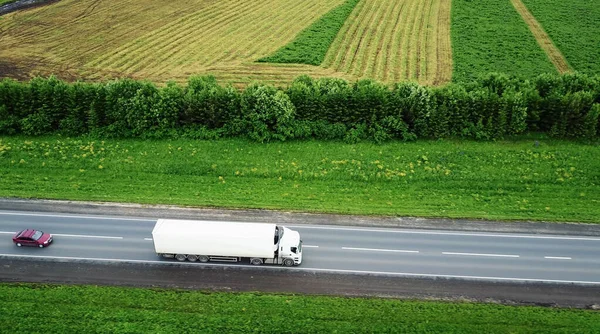 Vrachtwagens die naar de zon rijden. Luchtfoto van groene velden en vrachtwagens — Stockfoto