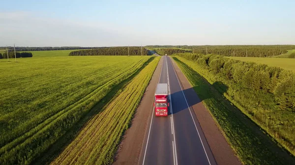 Vrachtwagens die naar de zon rijden. Luchtfoto van groene velden en vrachtwagens — Stockfoto