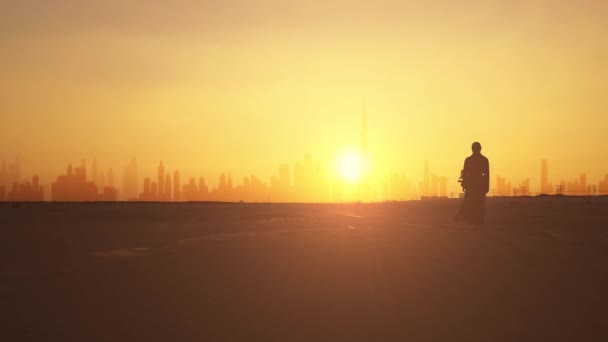 Mujer vestida de árabe tradicional se para en las montañas y levanta la mano. silueta de la ciudad de Dubai en el fondo — Vídeo de stock