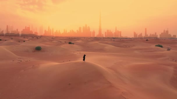 Frau in traditioneller arabischer Kleidung blickt auf die Silhouette der Stadt Dubai bei Sonnenuntergang. Starker Wind und kleiner Sandsturm. — Stockvideo