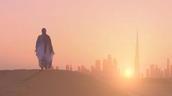 Mulher árabe vestida em vestido tradicional dos Emirados Árabes Unidos - abayain looks on the sunset at a desert with Dubai city silhouette on the background. — Fotografia de Stock