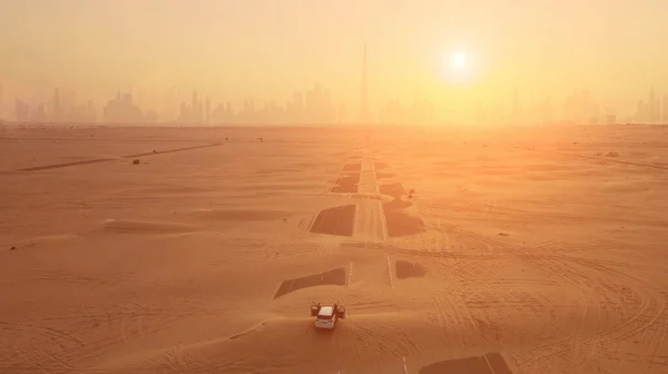 Colpo aereo. Coppia in macchina, si trova sulla strada dopo tempesta di sabbia. Silhouette Dubai città al tramonto. — Foto Stock