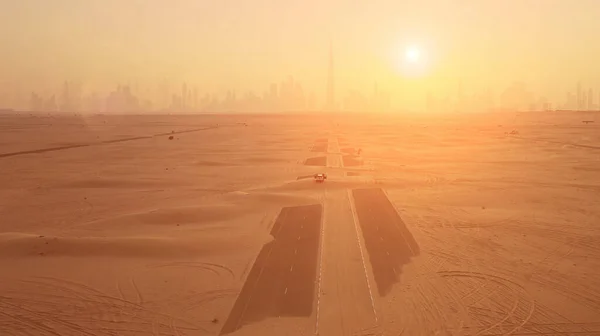 Colpo aereo. Coppia in macchina, si trova sulla strada dopo tempesta di sabbia. Silhouette Dubai città al tramonto. — Foto Stock