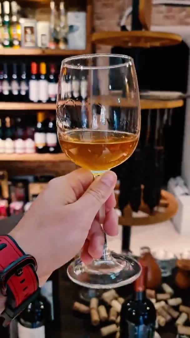 Αργή κίνηση POV αρσενικό χέρι που κατέχουν ποτήρι κρασιού με φόντο την αγορά κρασιού. — Αρχείο Βίντεο