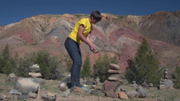 En resenär sätter en pyramid av stenar mot bakgrund av vackra berg. — Stockvideo