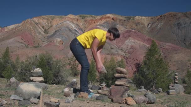 En resenär sätter en pyramid av stenar mot bakgrund av vackra berg. — Stockvideo