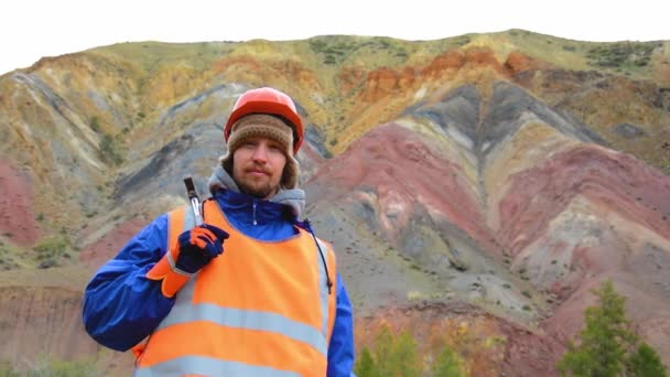 Porträtt av en gruvingenjör, geolog i skyddsväst, handskar och hjälm, med hammare i handen. — Stockvideo