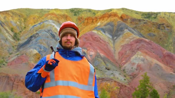 Портрет горного инженера, геолога в защитном светоотражающем жилете, перчатках и шлеме, с молотком в руке. — стоковое видео