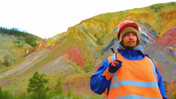 Porträtt av en gruvingenjör, geolog i skyddsväst, handskar och hjälm, med hammare i handen. — Stockvideo