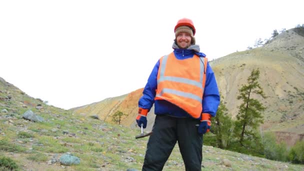 Porträtt av en gruvingenjör, geolog i skyddsväst, handskar och hjälm, med hammare i handen. — Stockvideo