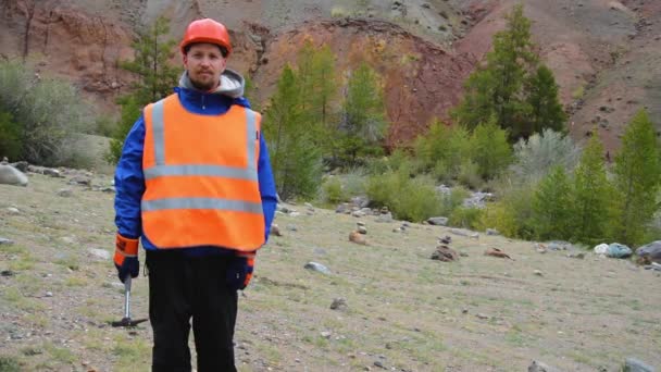 Portrait of a mining engineer, a geologist in the protective reflective vest, gloves and helmet, with hammer in hand. — Stock Video