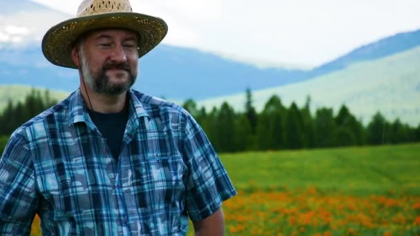 Hasır şapkalı bir çiftçi yüksek bir dağ tarlasının arka planında çiçeklerle — Stok video
