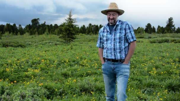 Hombre agricultor en un sombrero de paja sobre un fondo de un campo de alta montaña con flores — Vídeos de Stock