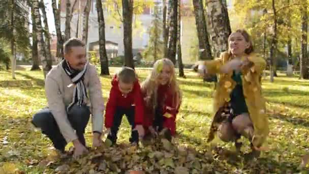 Портрет счастливой семьи в осеннем парке. Родители и дети подбрасывают оранжевые листья в воздух — стоковое видео