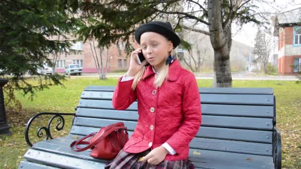 Fata vorbind pe telefonul inteligent stând într-un parc pe o bancă de lemn. Scena naturii . — Videoclip de stoc