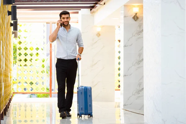 若いビジネスマンが荷物を持って歩き ホテルの廊下でスマートフォンを使用し スペースをコピー — ストック写真