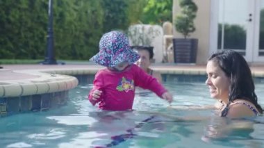 Anne küçük kızın havuza girmesine yardım ediyor.