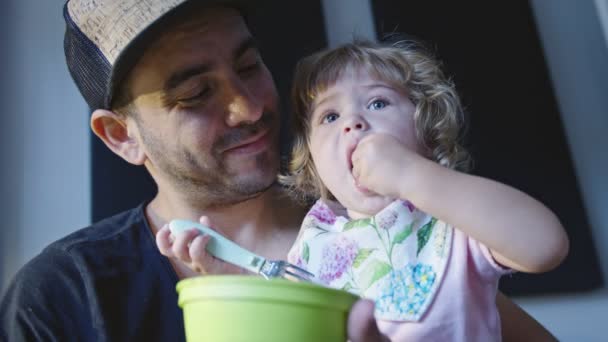 Klein meisje zitten in vaders schoot tijdens het eten met haar handen — Stockvideo