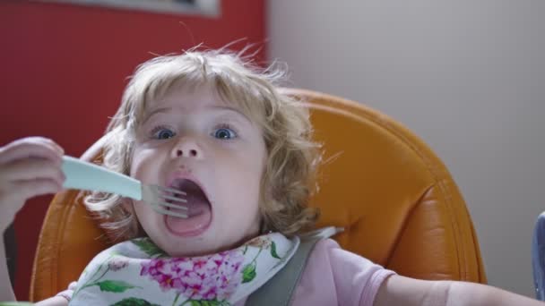 Mädchen macht lustiges Gesicht, spielt während der Fütterungszeit mit Gabel — Stockvideo