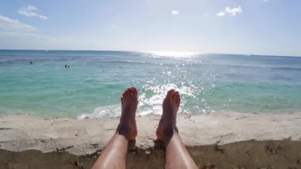 Los pies del hombre relajándose junto al océano en un día soleado con cielo azul claro — Vídeos de Stock