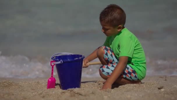 Barn leker med spade på stranden framför havet — Stockvideo