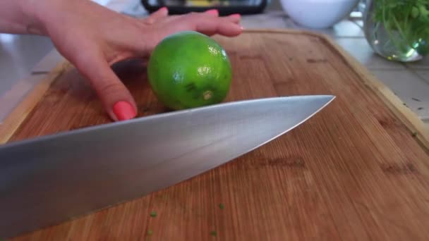 Mãos femininas cortando um limão verde ao meio com uma faca grande — Vídeo de Stock