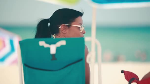 Mujer sentada en silla de playa y hablando frente al océano en un hermoso día — Vídeo de stock