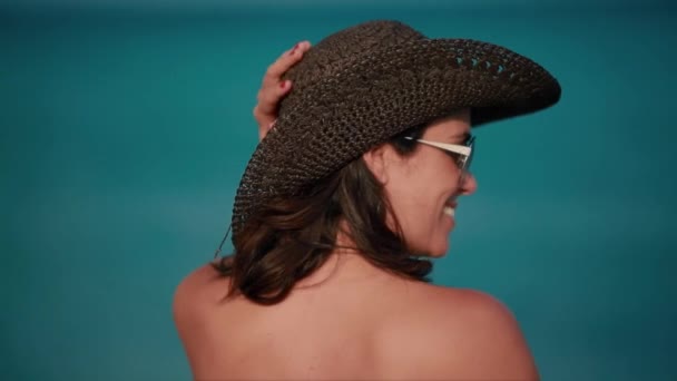 Piękna kobieta uśmiechając się naprzeciwko oceanu z plaży kapelusz — Wideo stockowe