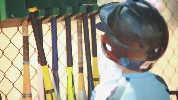 Niño dentro dugout en frente de los murciélagos durante el partido de béisbol — Vídeo de stock