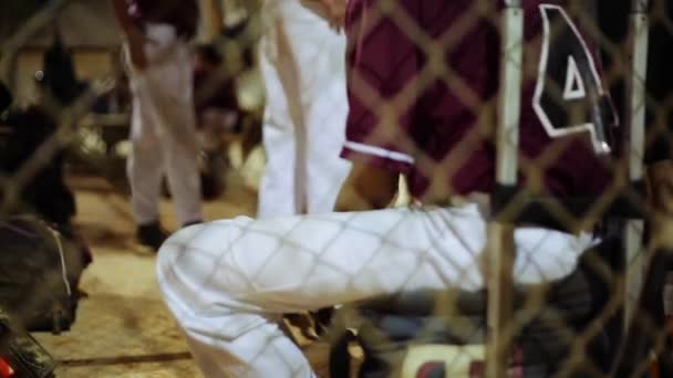 Jovem jogador de beisebol sentado dentro de um dugout e jogando com uma bola — Vídeo de Stock
