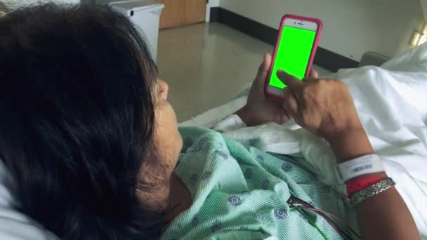 Mujer desplazándose a través de un teléfono inteligente mientras se acuesta en la cama del hospital — Vídeo de stock