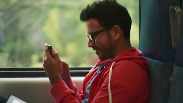 Человек, использующий свой мобильник и улыбающийся изнутри движущегося поезда — стоковое видео