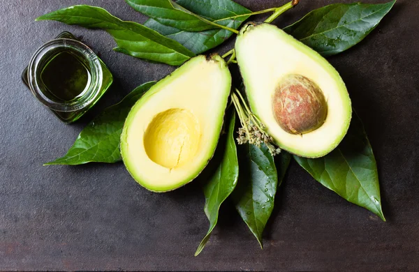 Aguacate con hojas y frasco de aceite verde. fondo negro —  Fotos de Stock