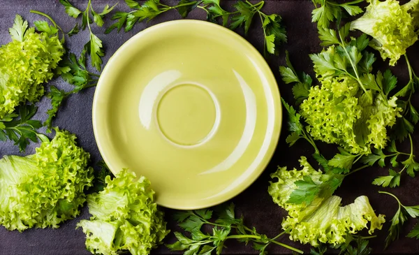 Świeże zioła sałata wokół zielony talerz na czarnym tle — Zdjęcie stockowe