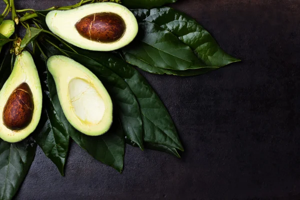 Aguacate fresco con hojas sobre fondo negro — Foto de Stock