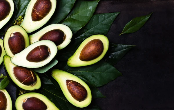 Verse avocado met bladeren op zwarte achtergrond — Stockfoto