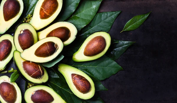 Aguacate fresco con hojas sobre fondo negro — Foto de Stock