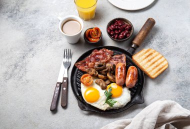 Izgara tavada kızarmış yumurta, sosis, pastırma, fasulye, tost, domates ve mantarla İngiliz kahvaltısı, somut arka plan, Top view.