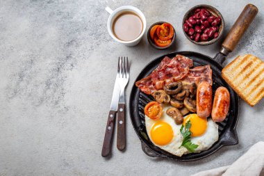 Izgara tavada kızarmış yumurta, sosis, pastırma, fasulye, tost, domates ve mantarla İngiliz kahvaltısı, somut arka plan, Top view.