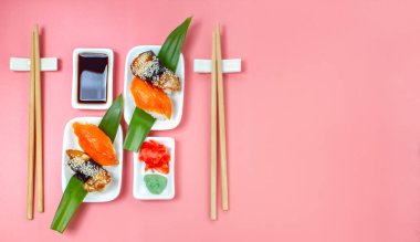 Yemek çubukları ve soya soslu suşi seti pembe minimalist arka planda..