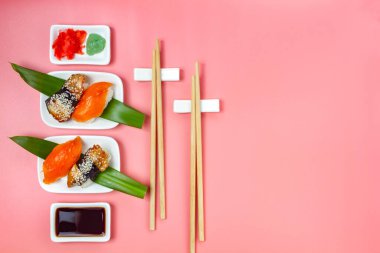 Yemek çubukları ve soya soslu suşi seti pembe minimalist arka planda..