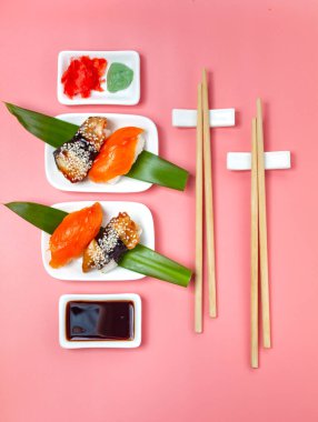 Yemek çubukları ve soya soslu suşi seti pembe minimalist arka planda..