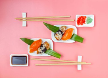 Yemek çubukları ve soya soslu suşi seti pembe minimalist arka planda..
