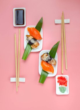 Yemek çubukları ve soya soslu suşi seti pembe minimalist arka planda..