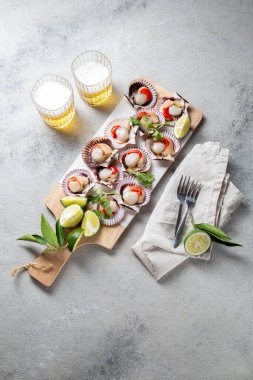 Çiğ deniz ürünleri, limonlu midye, kişniş ve michelada birası beyaz panoda, gri arka planda.