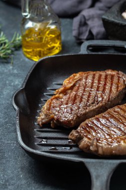Kızarmış biftek, dökme demir ızgara tavasında zeytinyağı ve biberiye, siyah arka plan..