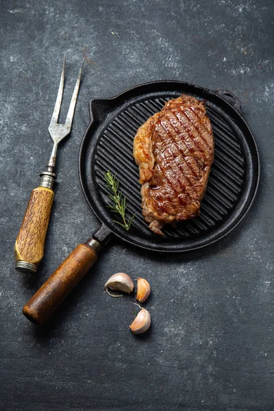 Stekt remsa loin biff på vintage gjutjärn grill pan och bestick set, svart bakgrund. Ovanifrån — Stockfoto