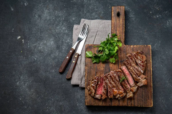 Stekt remsa loin biff på träskiva, svart bakgrund. Ovanifrån — Stockfoto