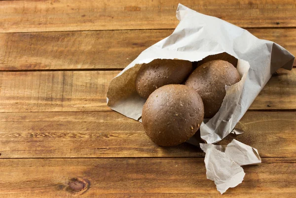 Rye bread in paper bag on wooden background.