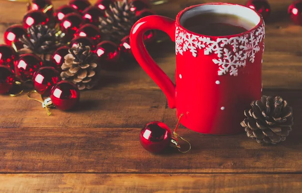 Xícara vermelha de chá e bolas de Natal no fundo de madeira — Fotografia de Stock